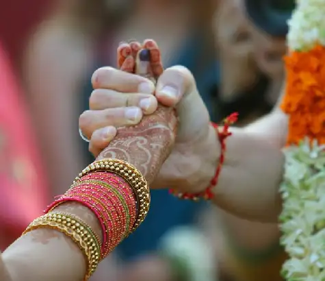 Couple holding hands with bangles and jasmine flowers during a wedding ritual